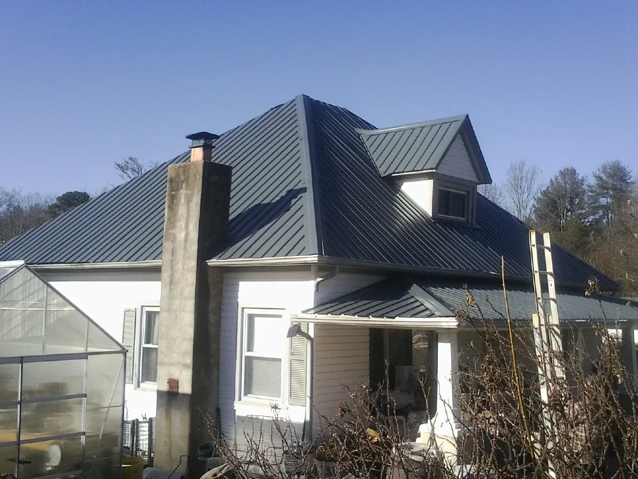 Dark blue standing seam metal roof on a white farmhouse with dormer — Slate & Tile Roof Repair by Roofing Brothers in Chancellor