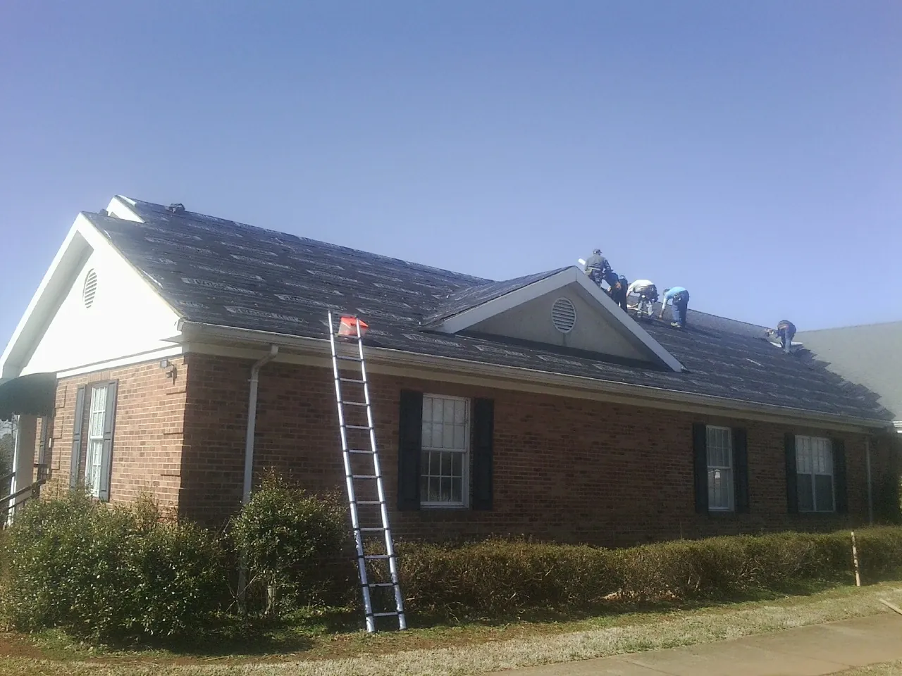 Crew tearing shingles off a brick ranch roof with a ladder set — Emergency Roof Repair work by our crew in Chancellor