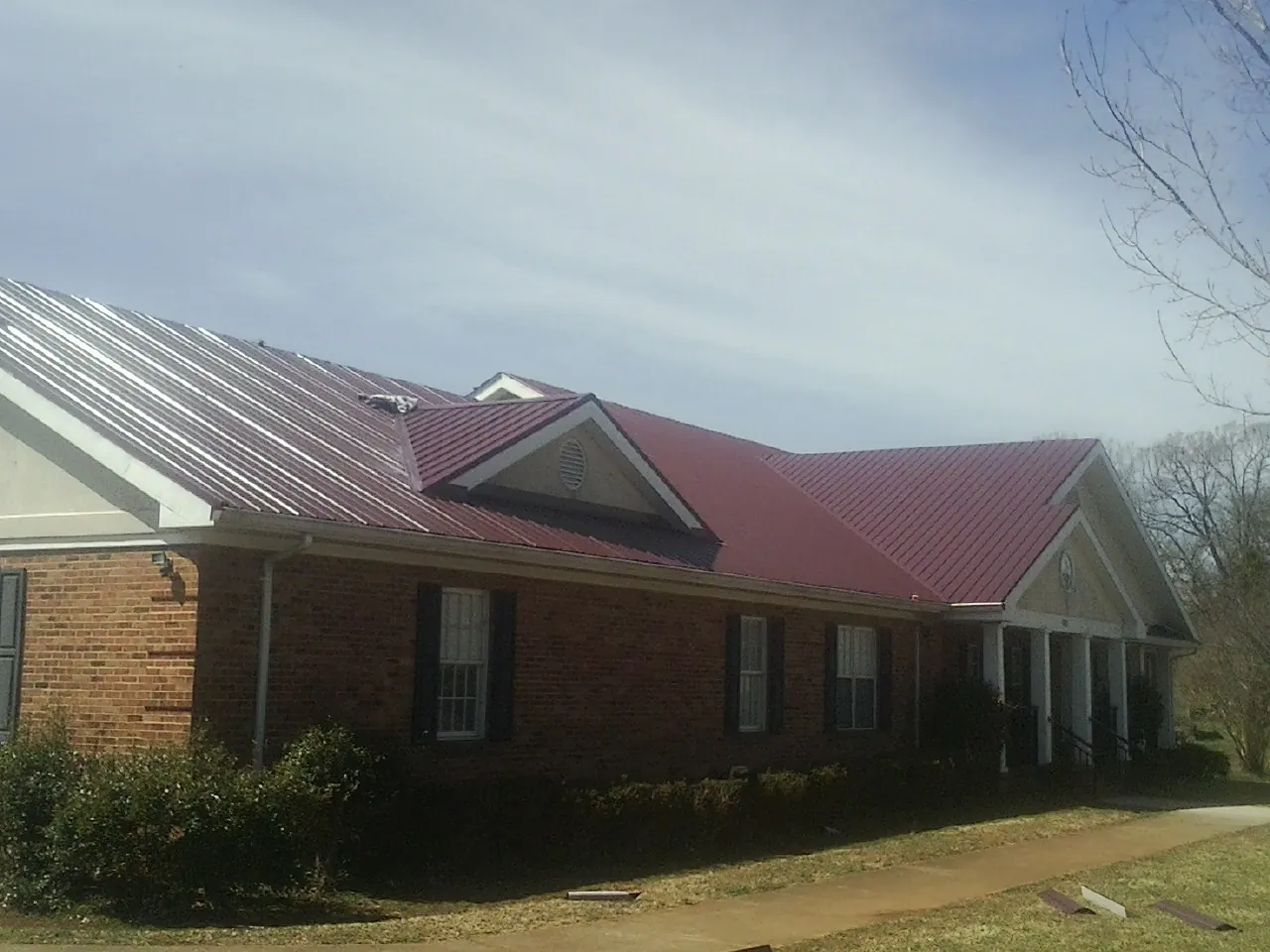 Red metal roof with gabled entries on a long brick building, from a Hail Damage Roof Repair job in Chancellor