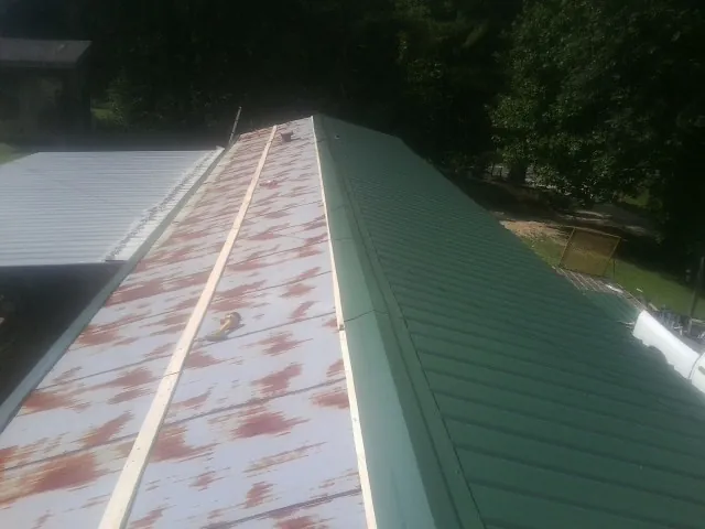 Old rusted panels beside newly installed green metal roofing — Wind Damage Roof Repair by Roofing Brothers in Chancellor