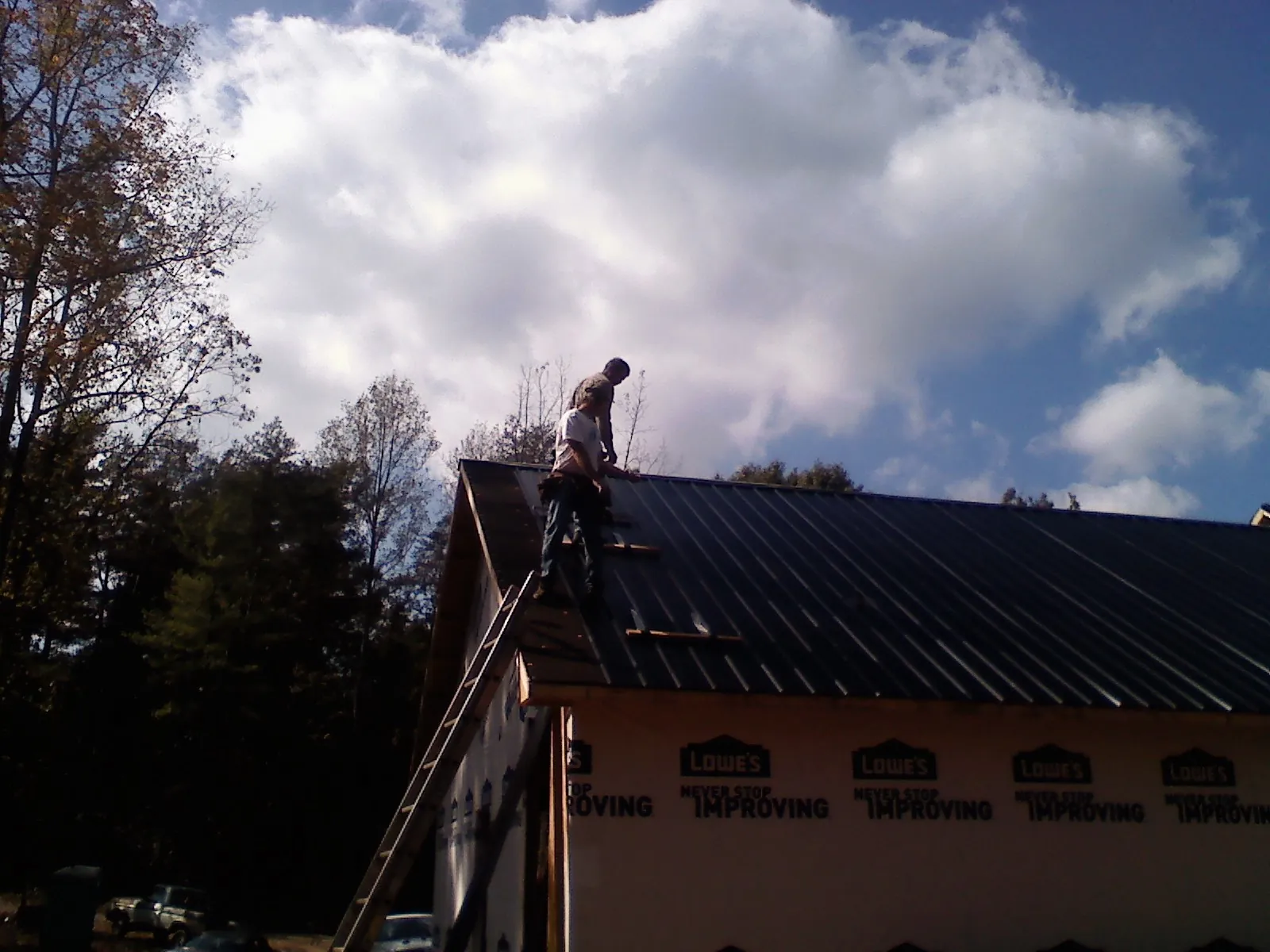 Roofer fastening dark metal panels high against a cloudy sky, from a Roof Inspection job in Chancellor